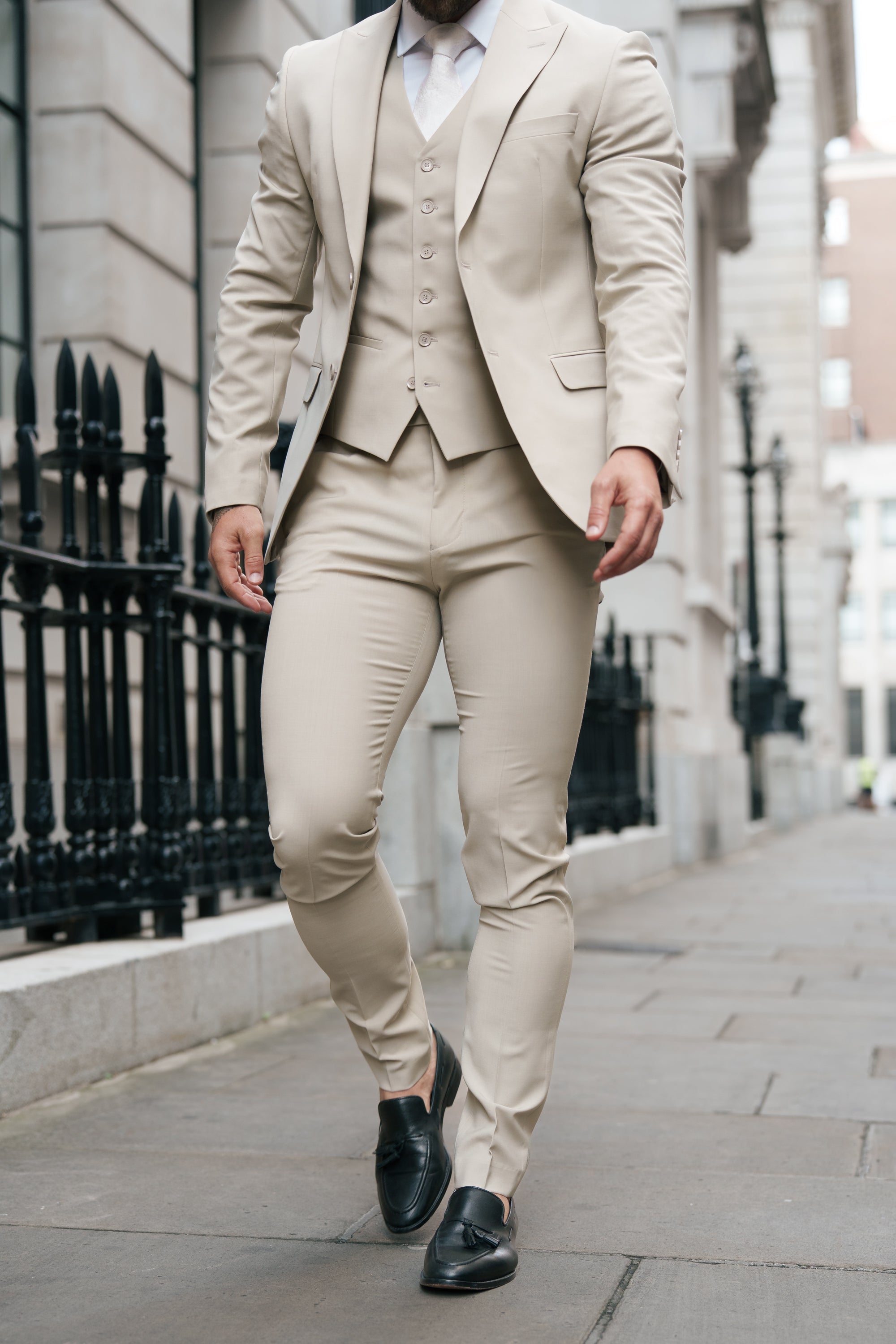 Man wearing a beige suit walking on a city street.