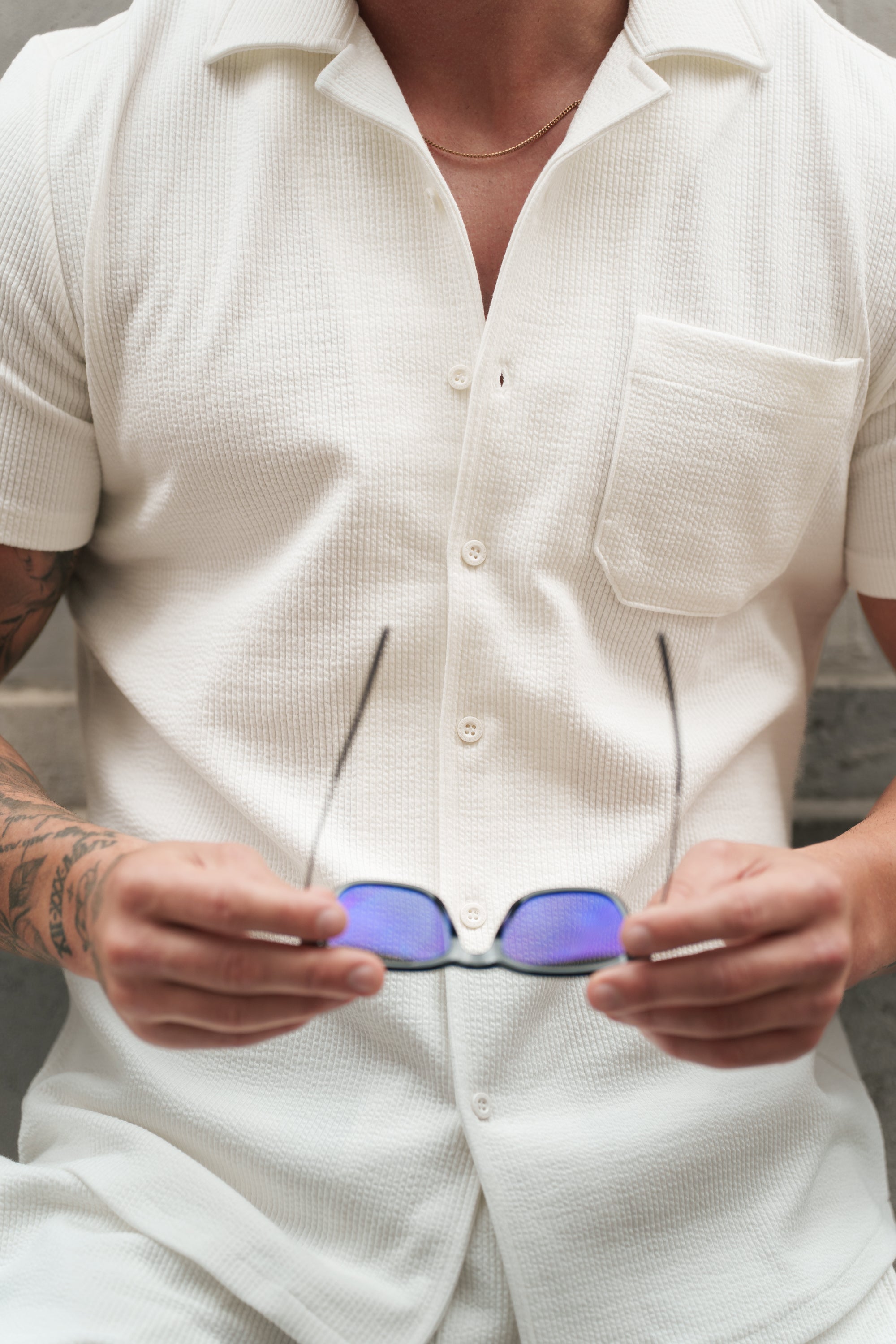 Person wearing a white shirt holding sunglasses with a blurred background