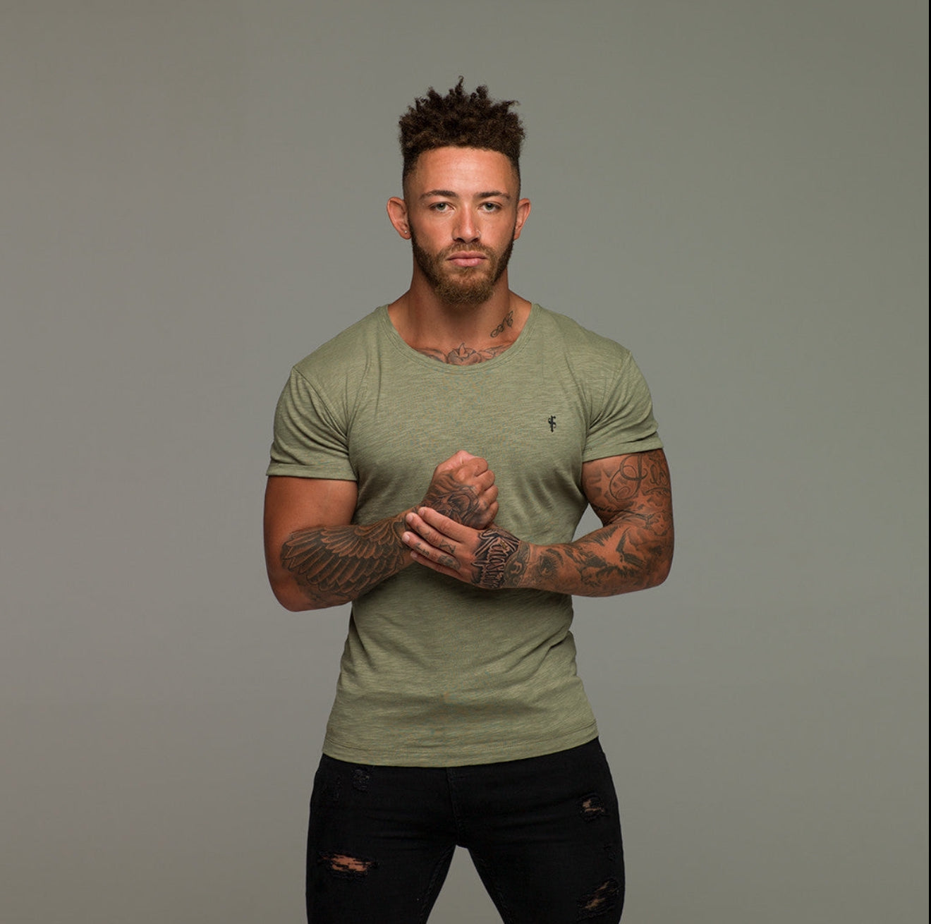 A man wearing a green Father Sons olive slub crew t-shirt with a silicone emblem on the front.