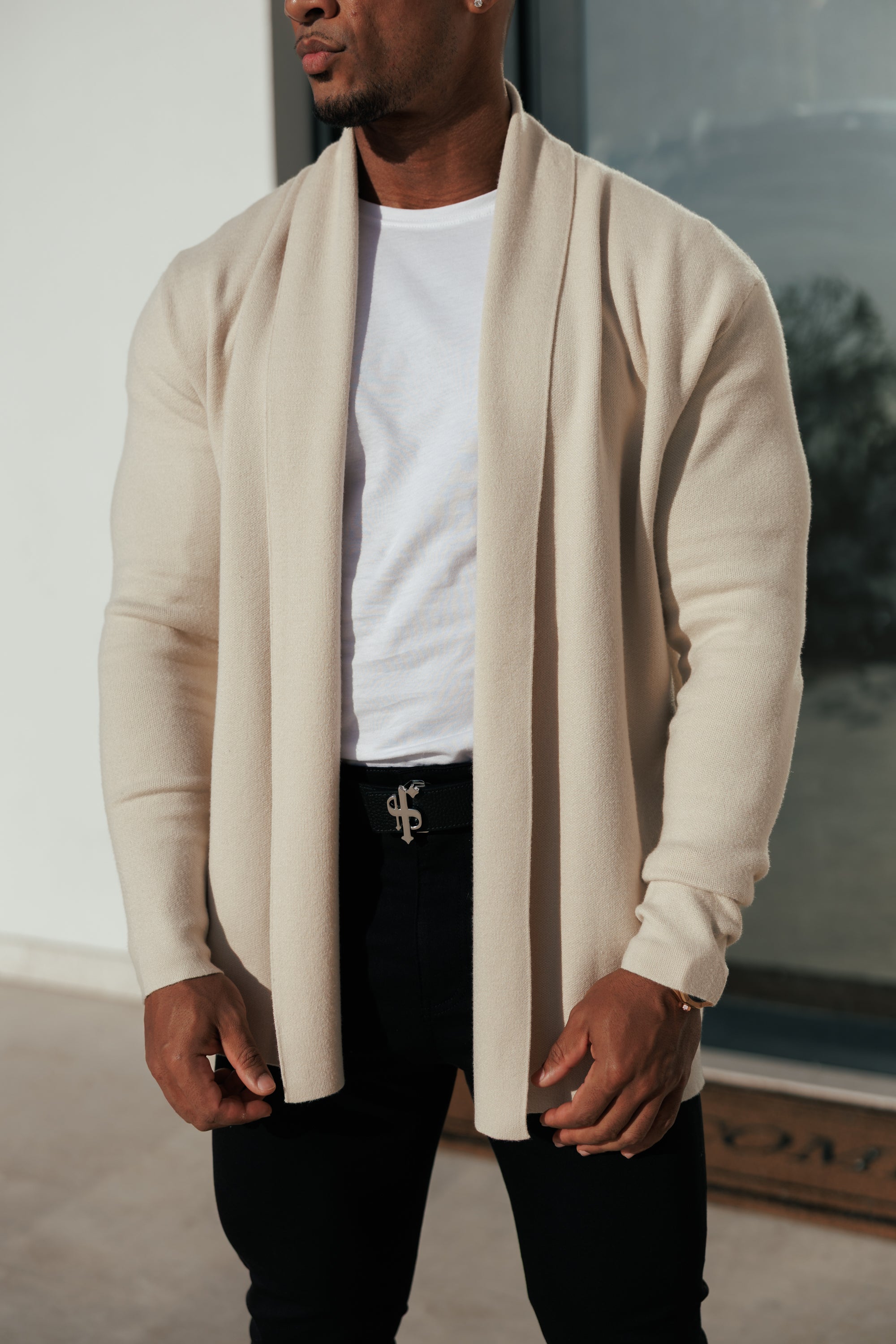 Man wearing a beige cardigan over a white shirt and black pants.