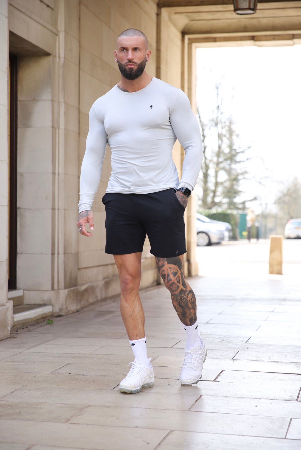 A man wearing a long sleeve stone grey gym crew top and black shorts.