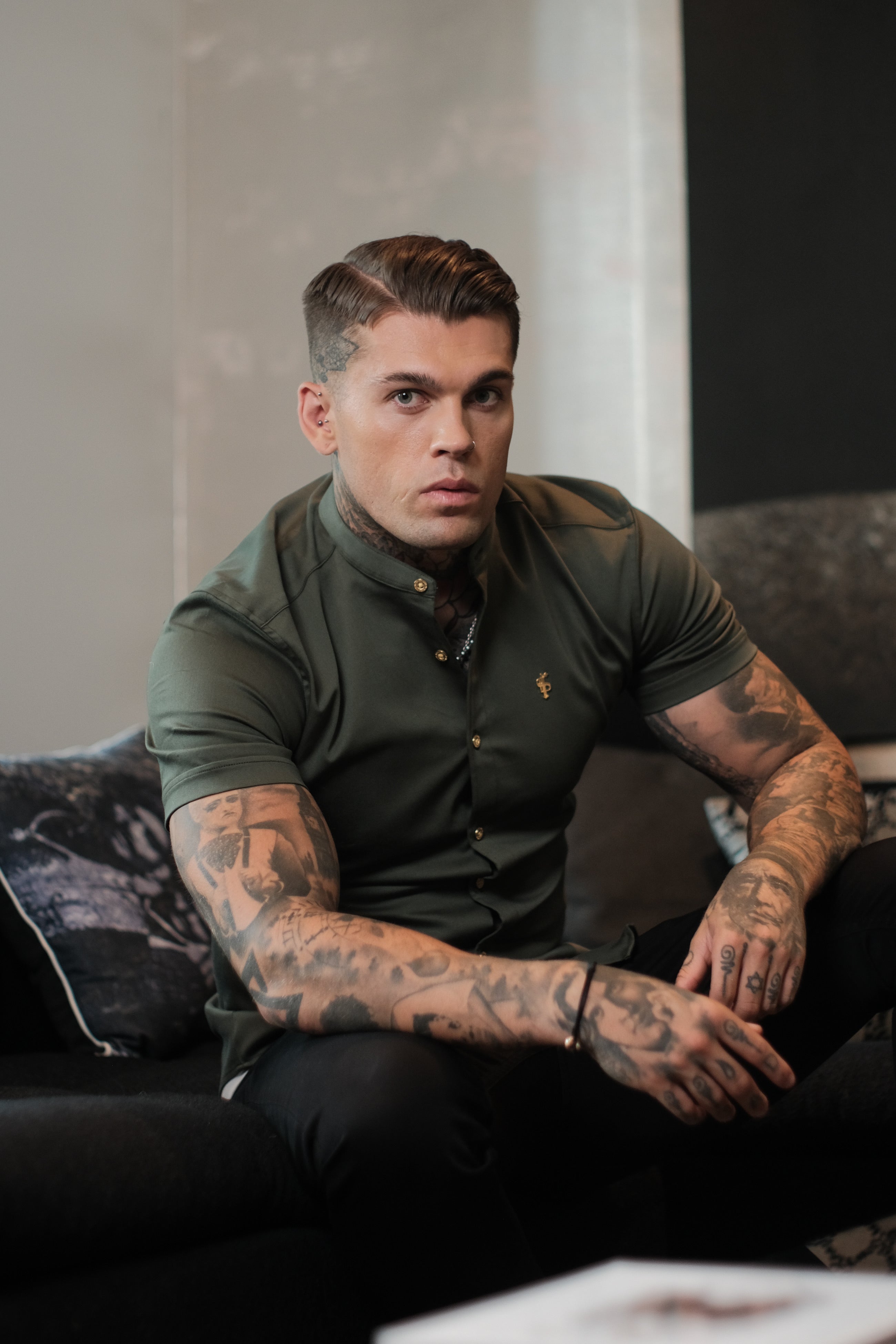 A male model wearing a short-sleeved khaki denim shirt with metal buttons and a grandad collar.