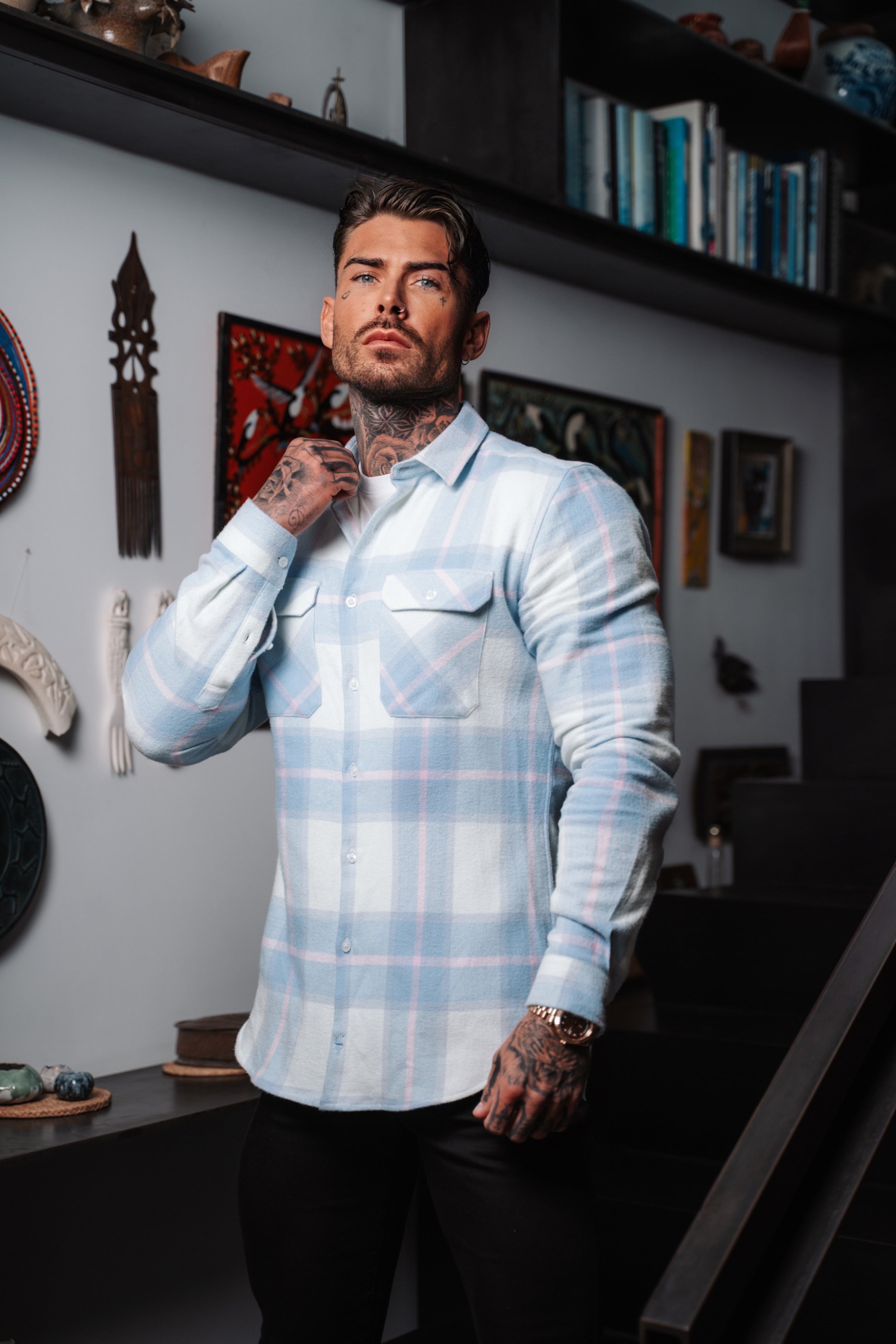 A man wearing a multi checkered long sleeve shirt in a room with various items displayed on the walls.