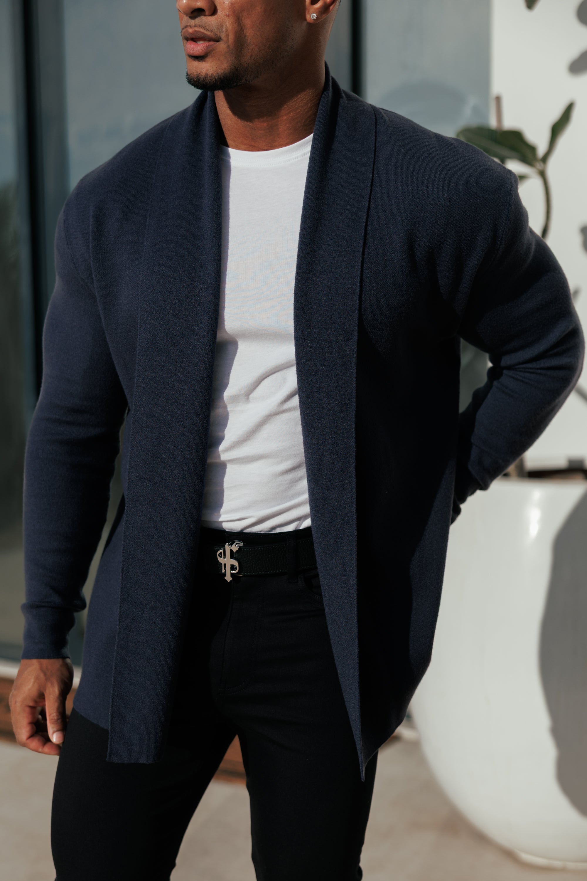 Man wearing a navy cardigan over a white shirt with black pants.