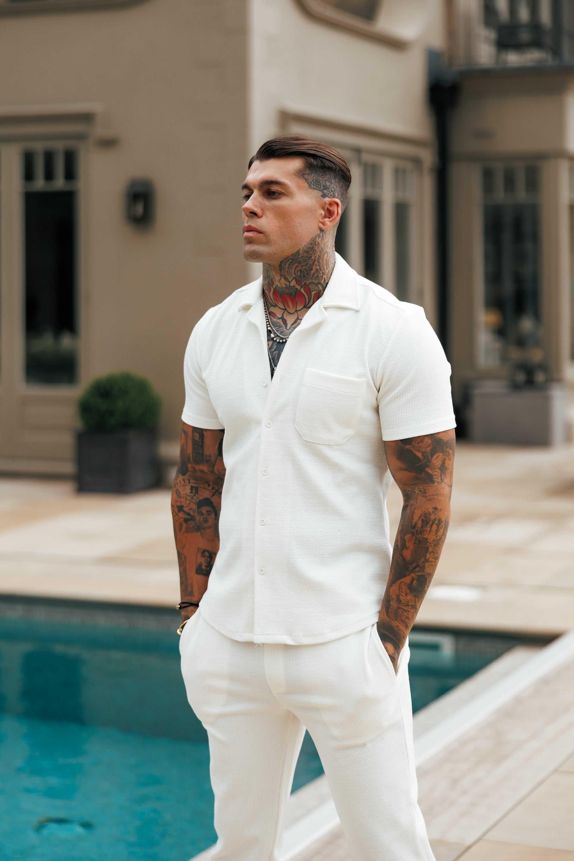 Man in a white outfit standing by a pool with a building in the background