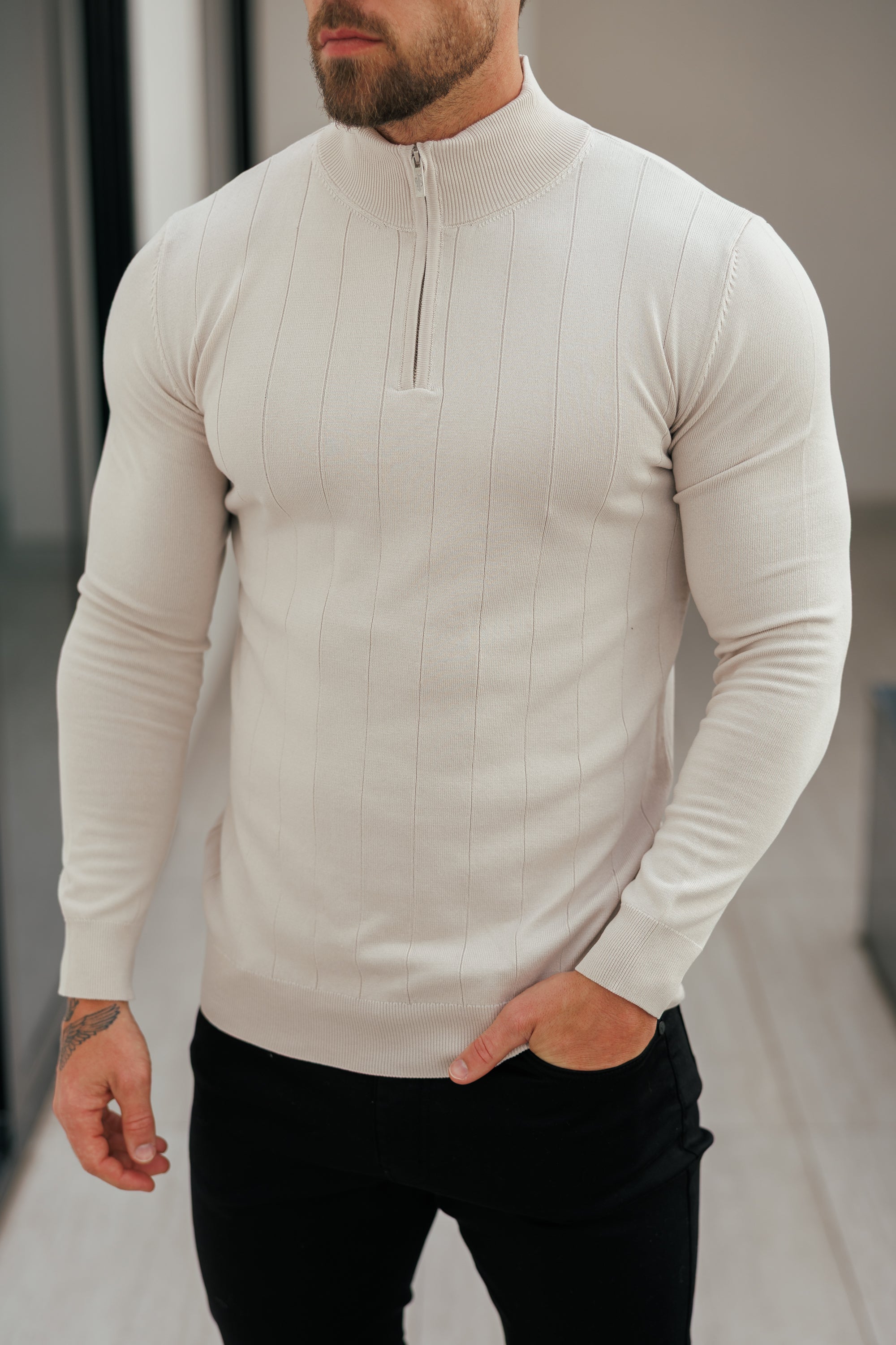Man wearing a beige long-sleeve shirt with a zipper detail, standing indoors.