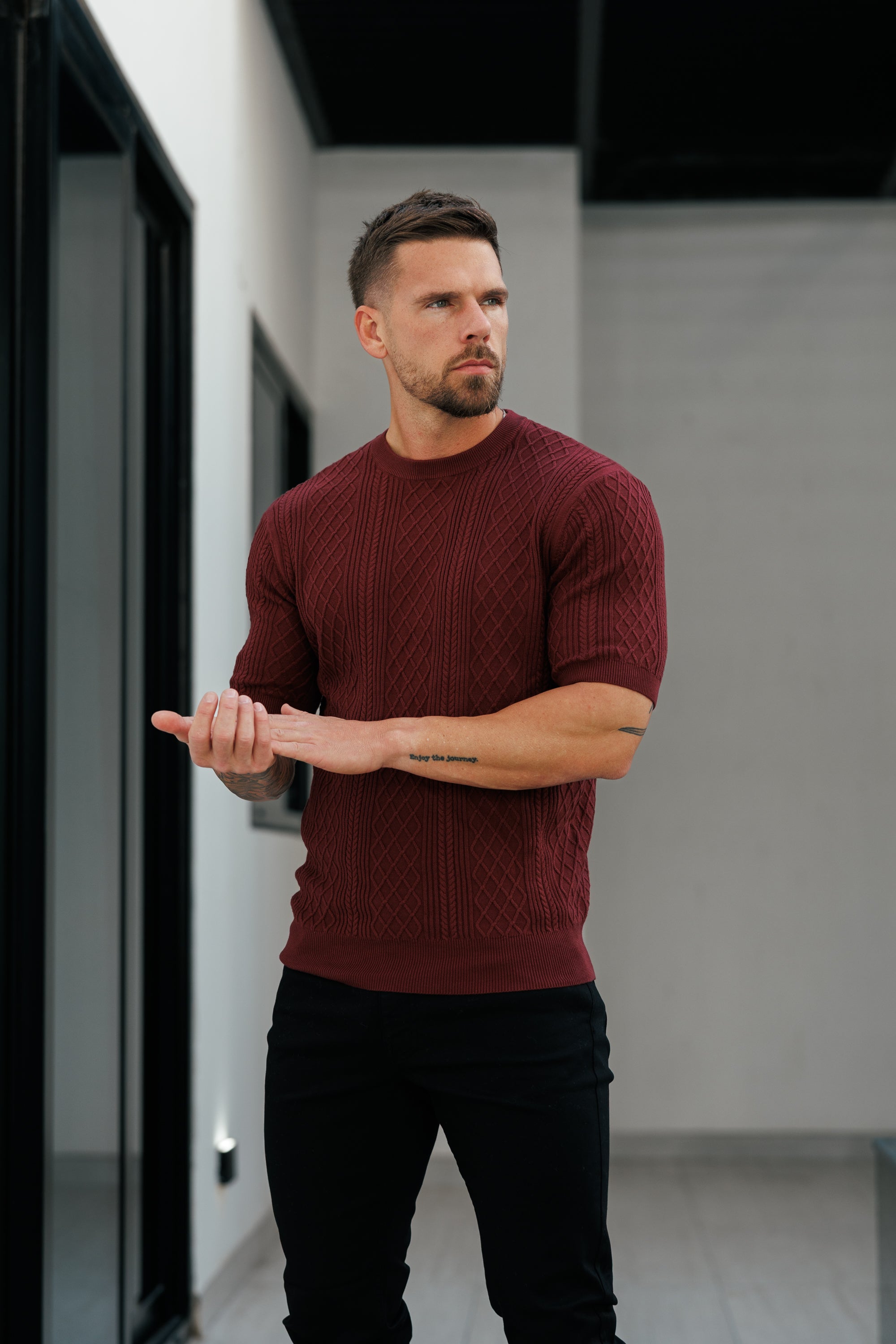 Man wearing a maroon sweater and black pants standing indoors.