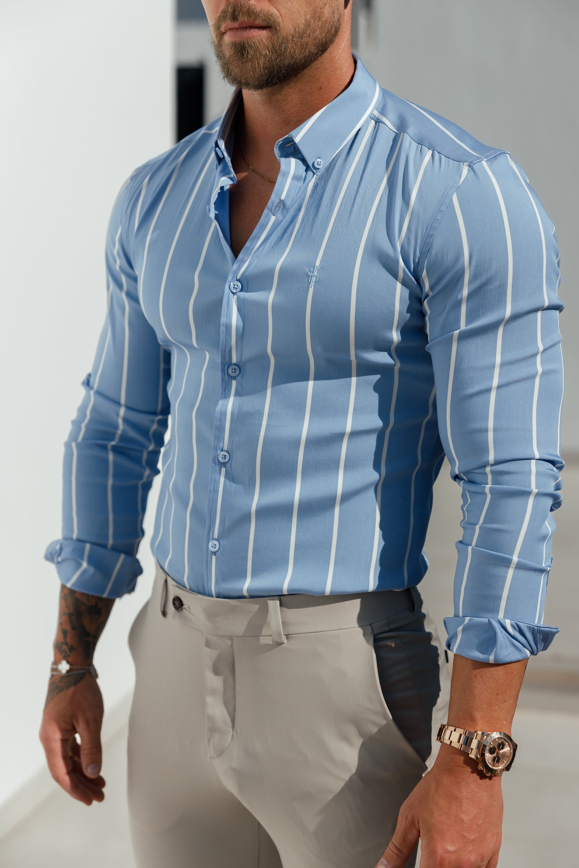 A man wearing a light blue long sleeve button-down shirt with wide vertical stripes and a collar.