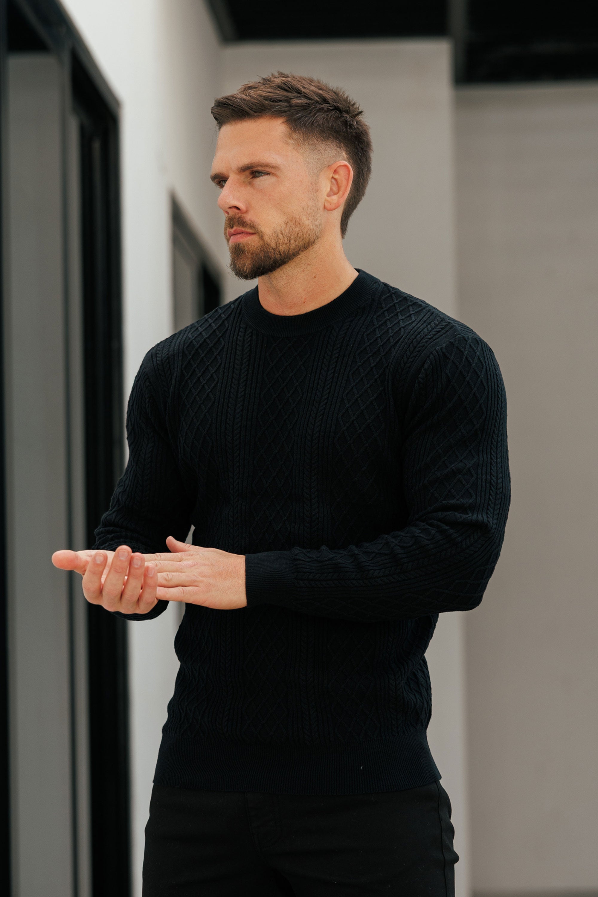 Man wearing a black sweater standing indoors with a neutral background