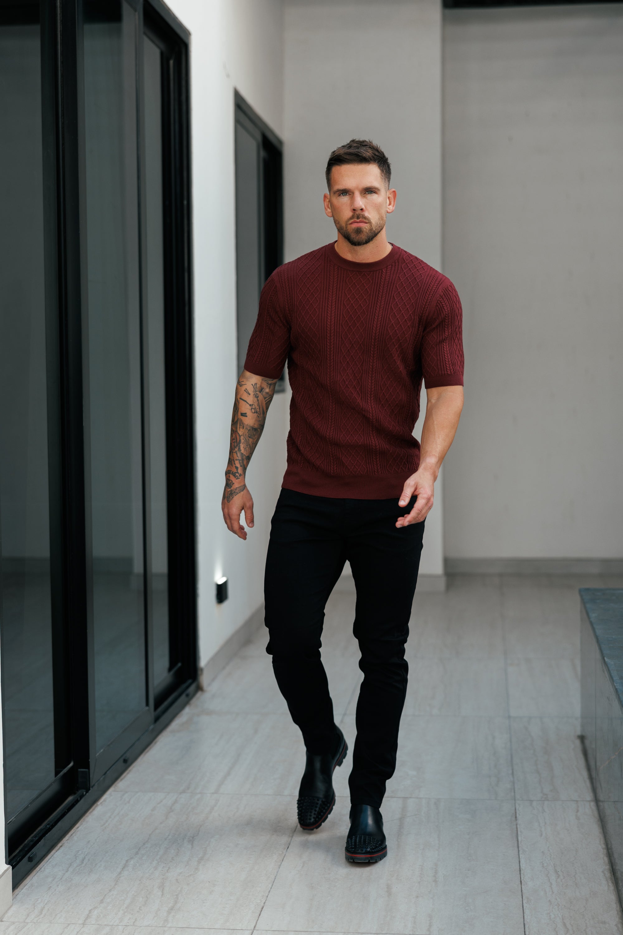 Man in a maroon sweater and black pants walking in a modern indoor setting
