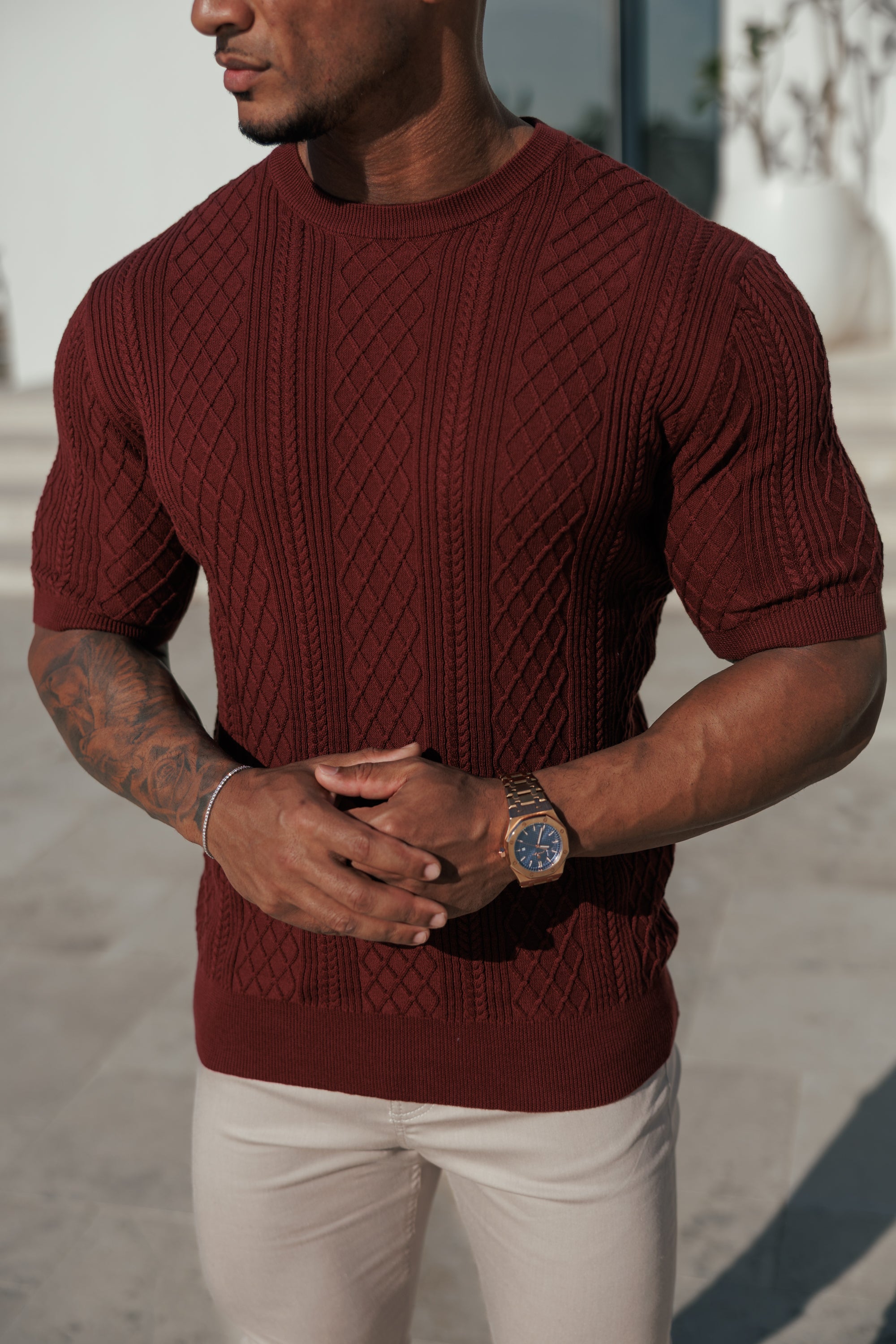Man wearing a maroon sweater and white pants with a blurred background